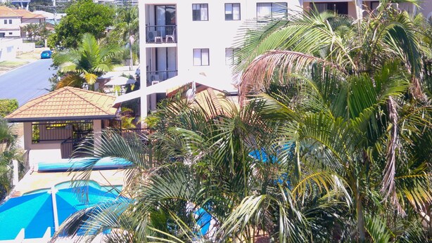 A residential building with a swimming pool, surrounded by palm trees and a city skyline in the background. - Chevron Palms Holiday Apartments by Gold Coast Premium (Surfers Paradise)