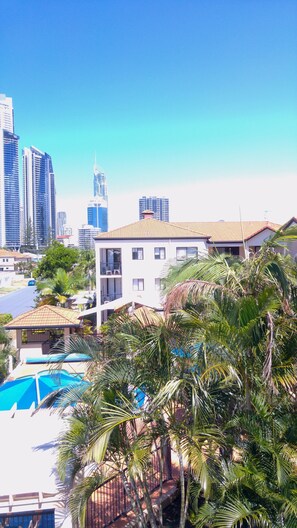 Um edifício residencial com piscina, cercado por palmeiras e um horizonte urbano ao fundo.
