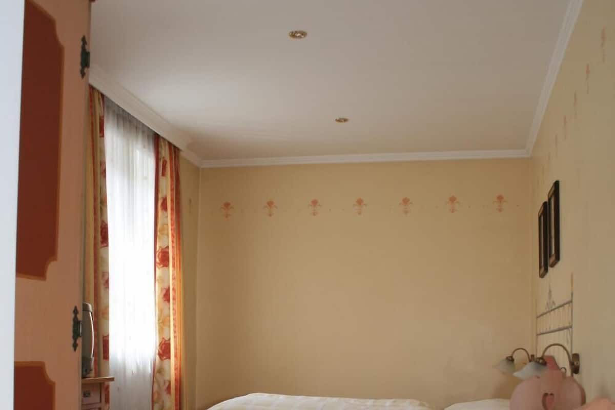 A bedroom with a bed, a chair, a desk, and a window with curtains.