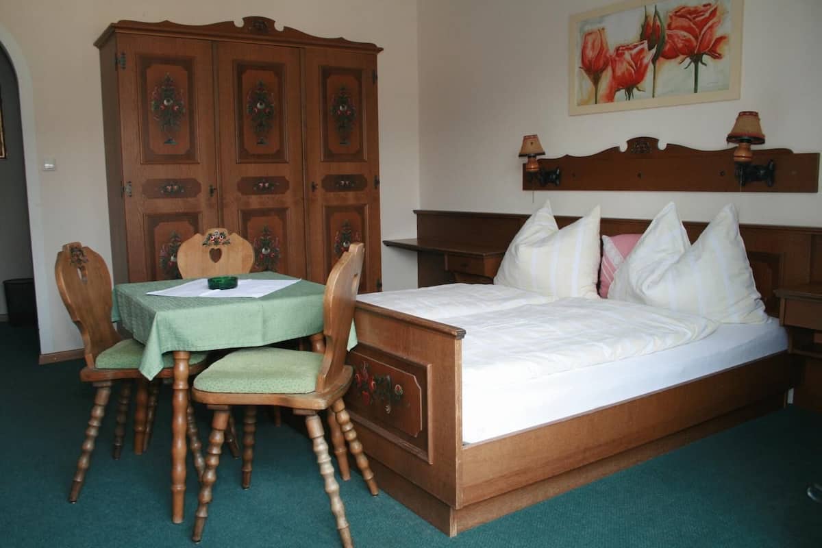 A bedroom with a wooden bed, a green table with chairs, and a large wooden wardrobe.