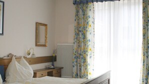 A bedroom with a wooden bed, a bedside table, a nightstand, a mirror, and a radiator. - Gasthof Goldener Stern (Sankt Koloman)