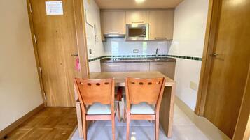 A compact kitchen with wooden cabinets, a microwave, and a sink. There are two wooden chairs and a small table.
