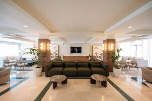 A spacious lobby with a central seating area, a flat-screen TV mounted on the wall, and a reception desk with a computer.