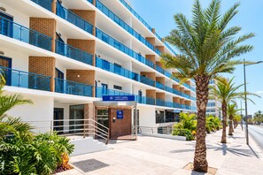Un hotel de varios pisos con diseño moderno, que cuenta con balcones, una entrada central y un cielo despejado.