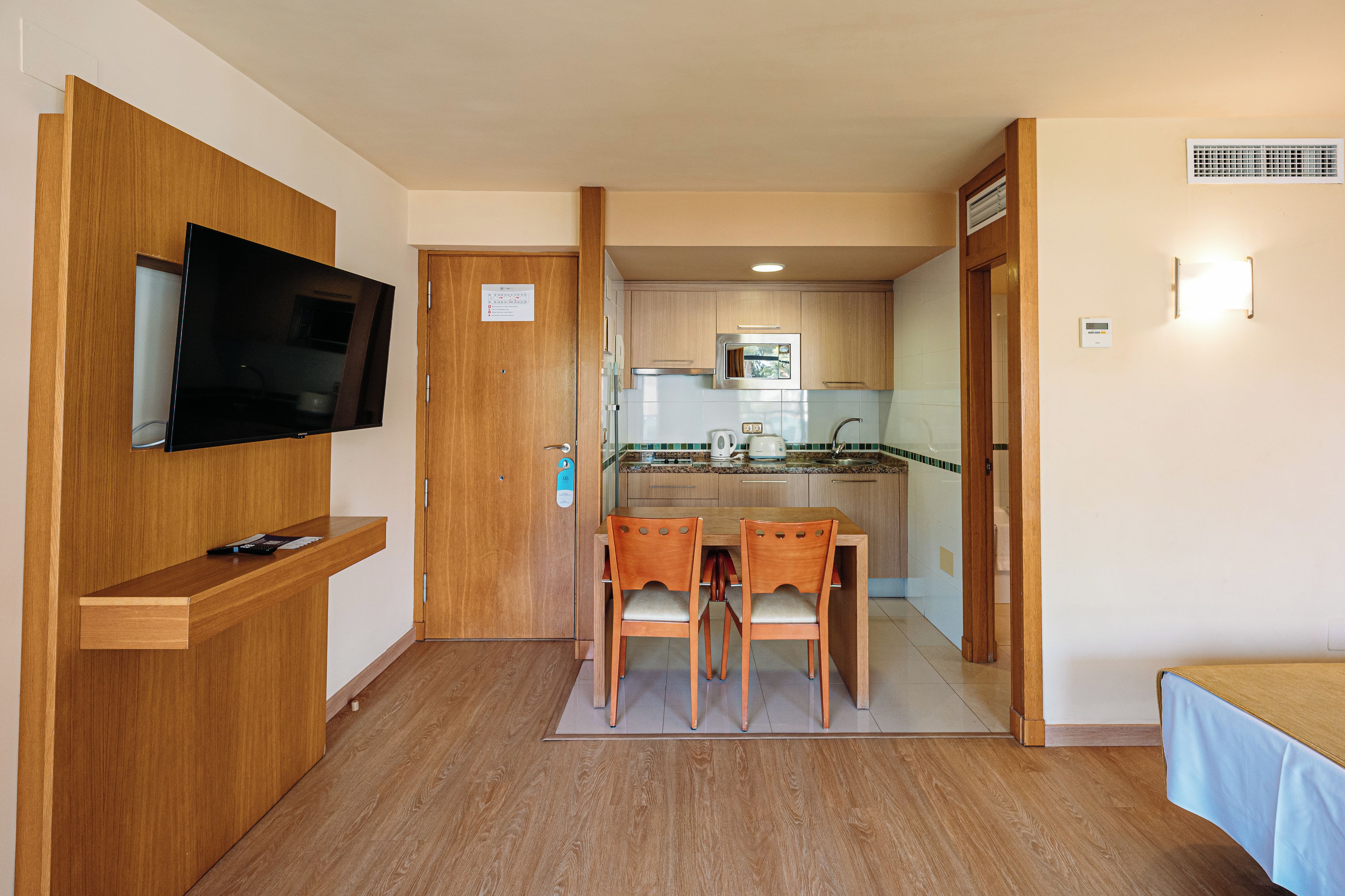 Habitación de hotel compacta con televisor, una pequeña mesa con sillas, kitchenette y baño.