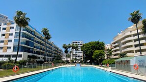 Een zwembad met helderblauw water, omgeven door moderne gebouwen met balkons en palmbomen.