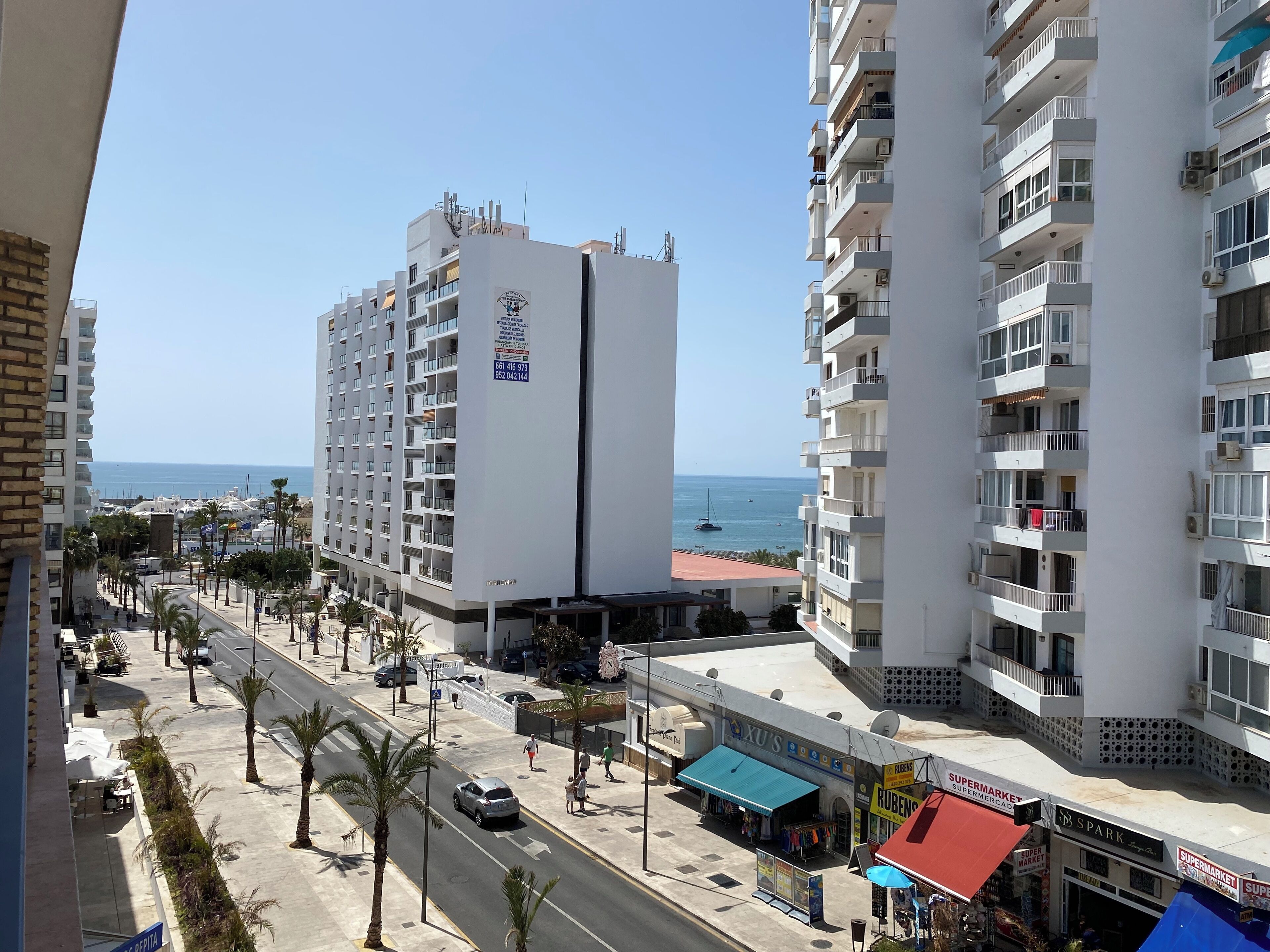 Un immeuble de grande hauteur doté de balcons, une rue bordée de palmiers et une vue sur la mer.