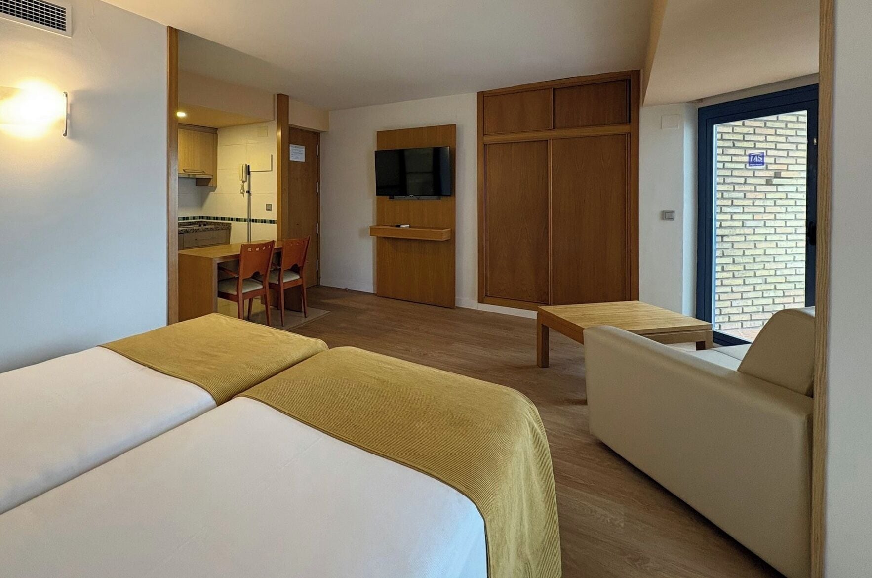 Une chambre d’hôtel avec deux lits, un canapé, une petite table, une télévision et une kitchenette.