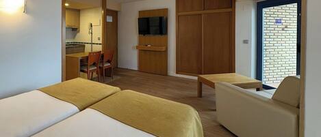 Une chambre d’hôtel avec deux lits, un canapé, une petite table, une télévision et une kitchenette.