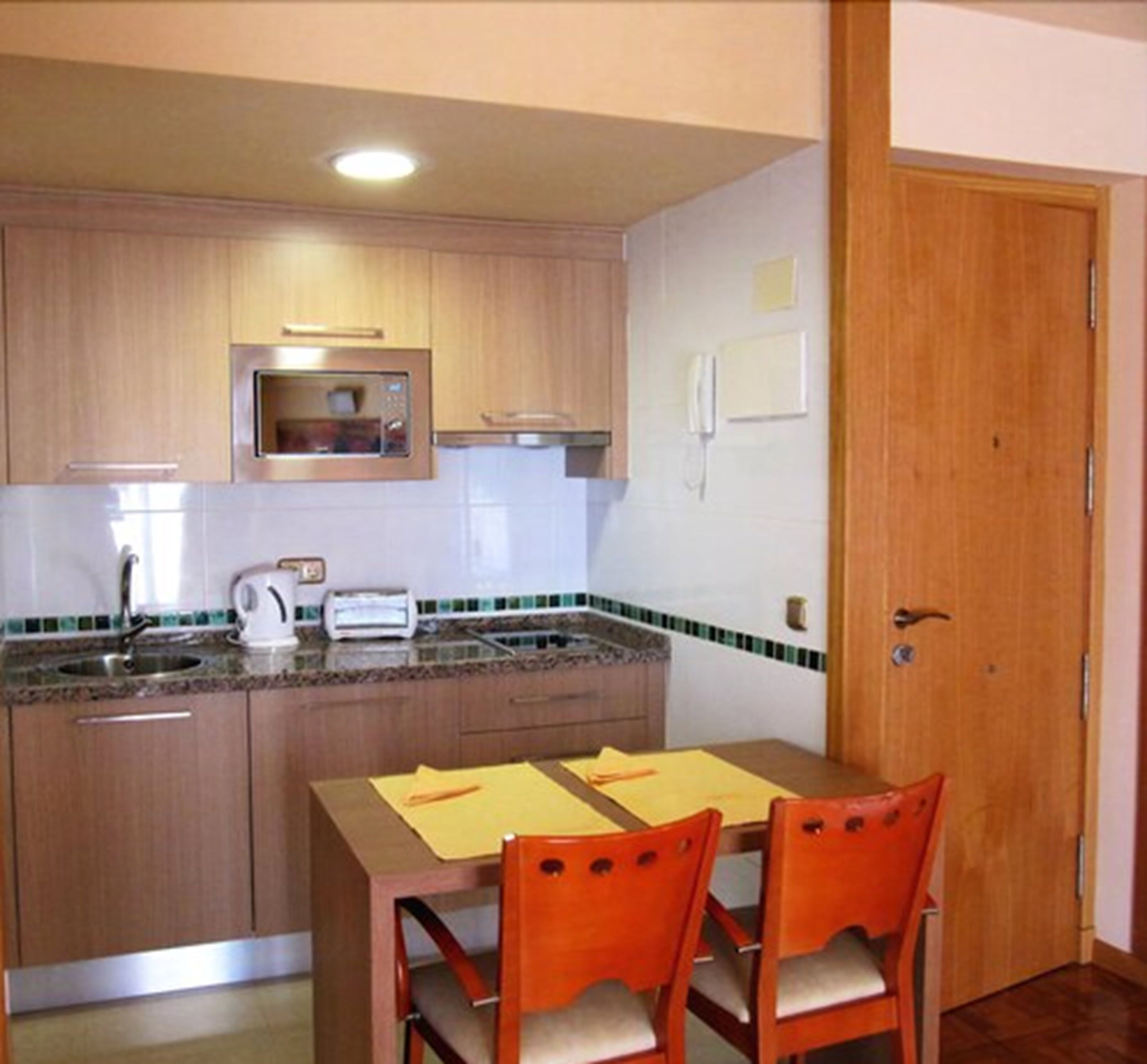 Una cucina compatta con mobili in legno, un forno a microonde, un lavandino e un tavolo da pranzo con due sedie.