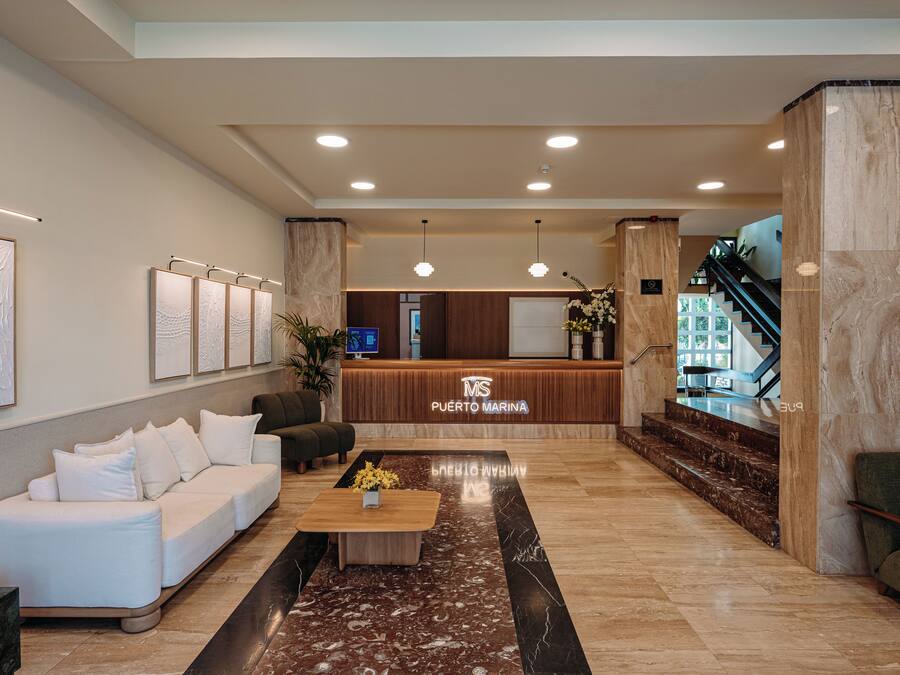 Un vestíbulo de hotel con mostrador de recepción, zona de estar y una escalera.