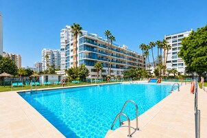A swimming pool with a clear blue water surface, surrounded by lounge chairs and palm trees.