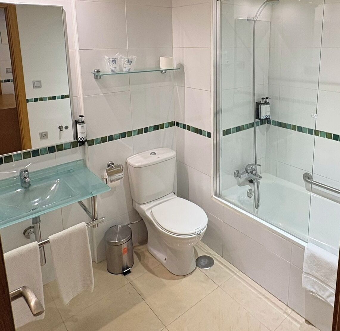 A modern bathroom with a glass shower enclosure, a glass sink, and a toilet.