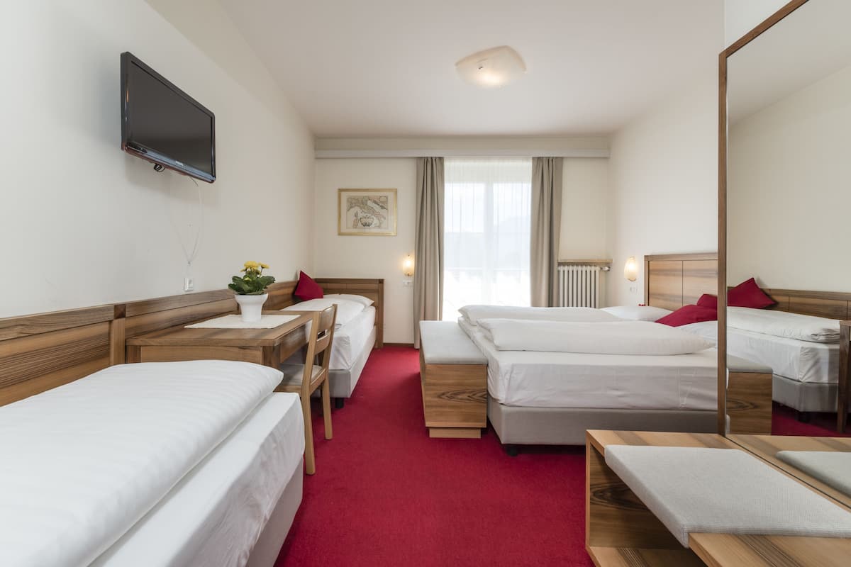 A hotel room with two single beds, a wooden nightstand, a bedside table, a TV mounted on the wall, a red carpet, and a window with curtains.