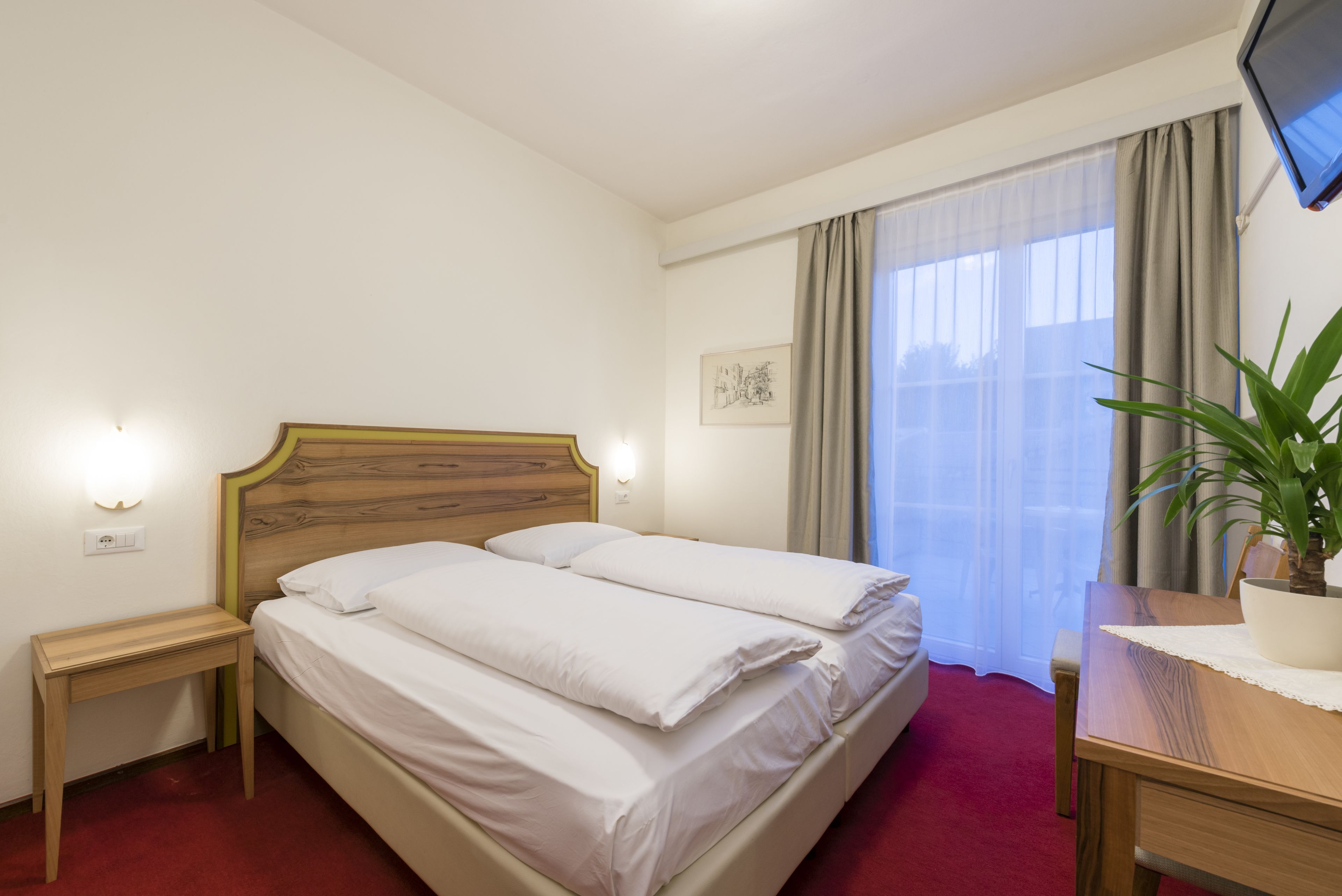 A hotel room with a bed, bedside tables, a TV, and a window with curtains.