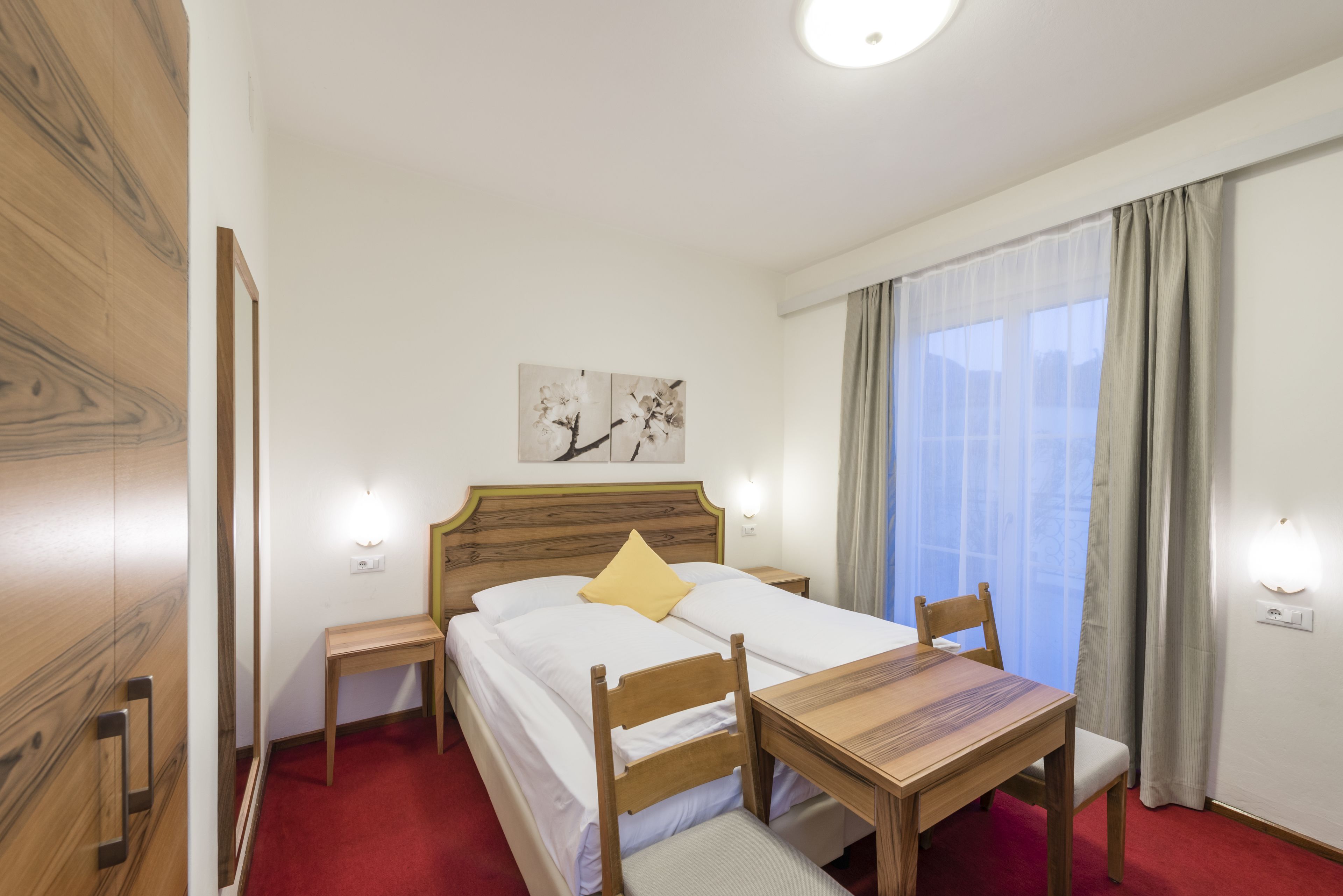 A hotel room with a bed, bedside table, chair, and a small table with a chair.