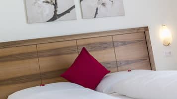 A neatly made bed with white linens and a single red pillow, a wooden headboard, and two wall-mounted light fixtures.