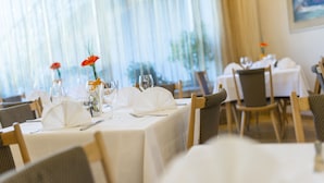 A dining area with tables set for two, featuring white tablecloths, neatly arranged cutlery, and small flower arrangements. - Elefant (Ora)