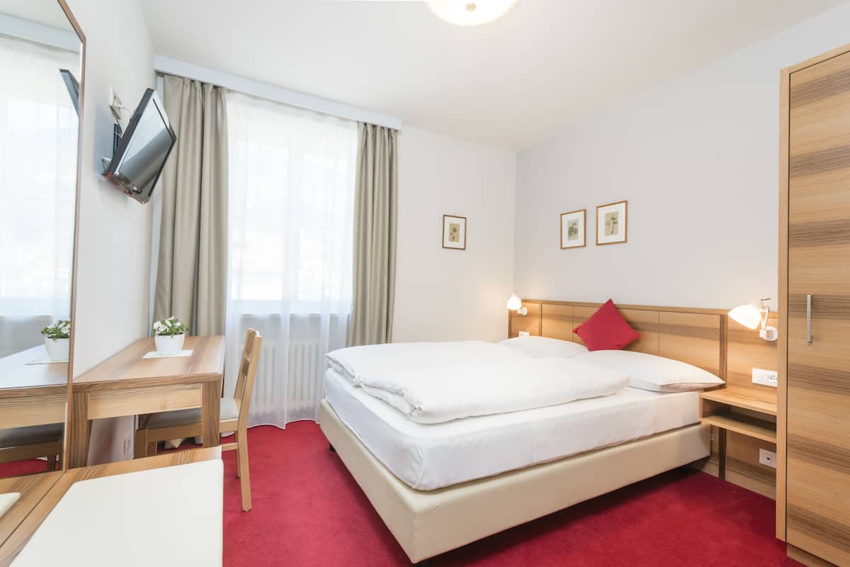 A hotel room with a bed, bedside table, lamp, and a desk with a chair.