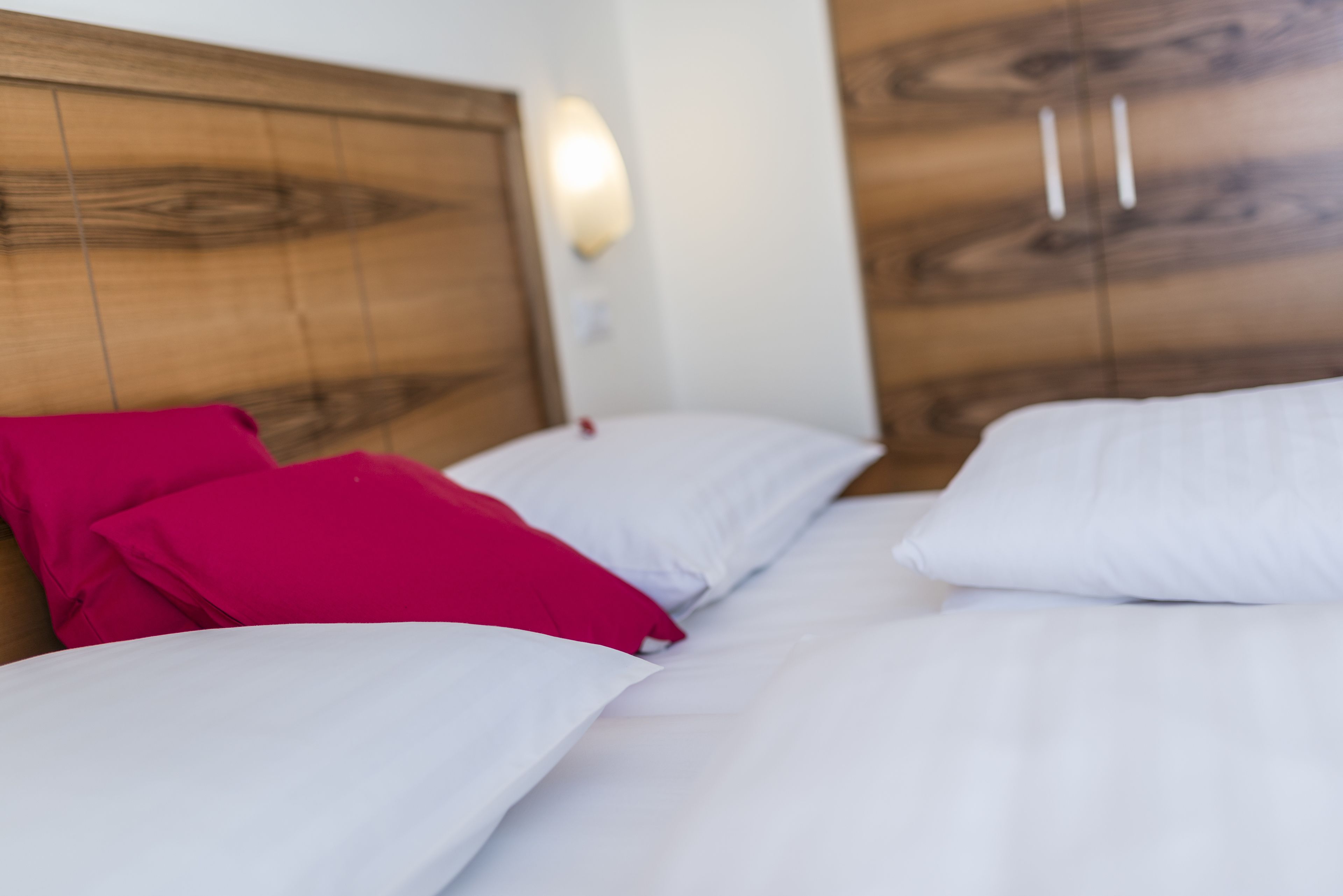 Un letto con cuscini bianchi e rosa, una testiera in legno e un lampadario fissato al muro.