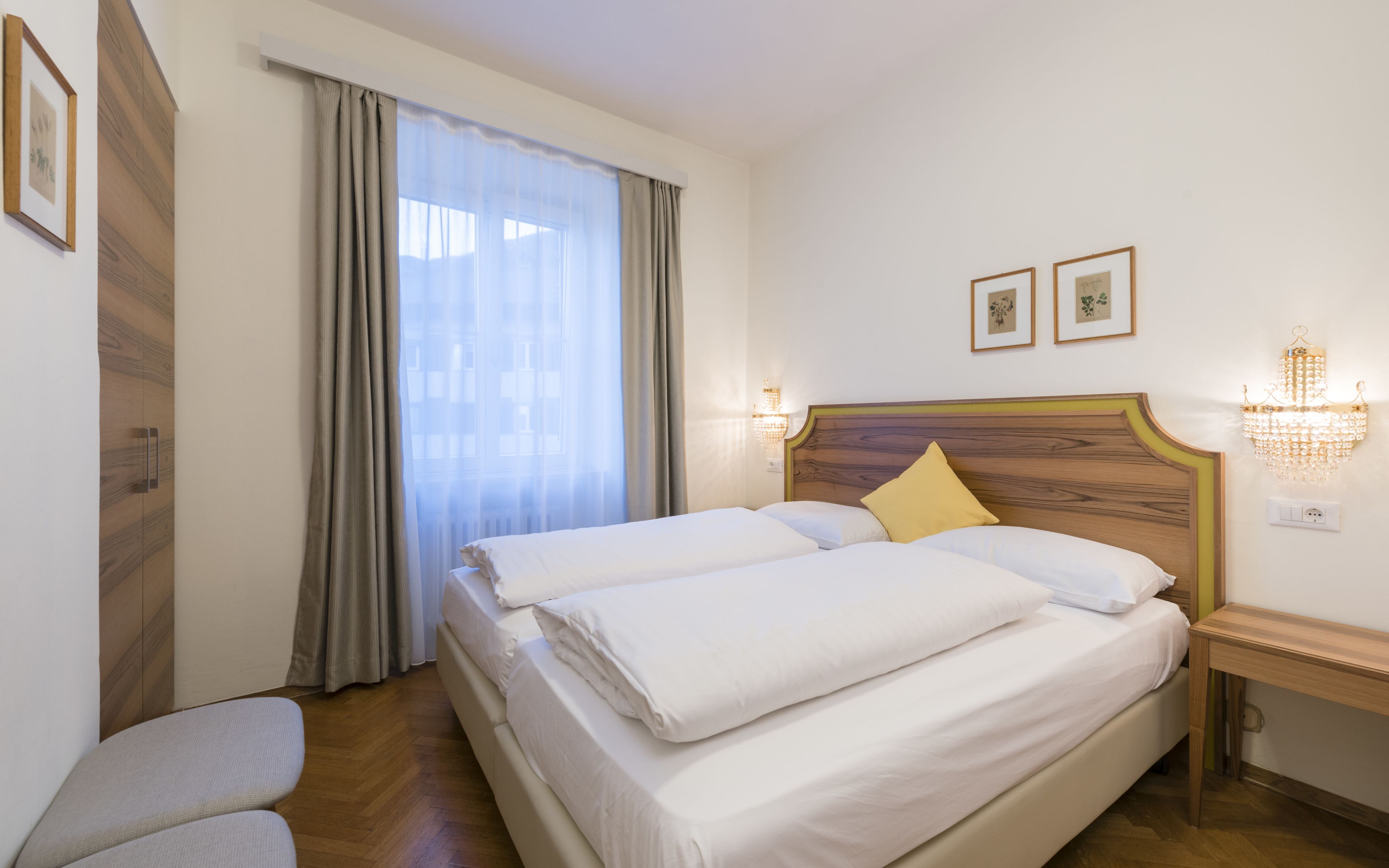 Ein Hotelzimmer mit einem großen Bett, einem Nachttisch, Vorhängen am Fenster und Wandleuchten.