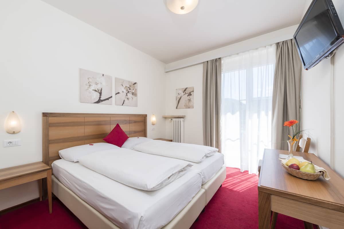 A hotel room with two beds, a desk with a fruit basket, a TV, and artwork on the walls.