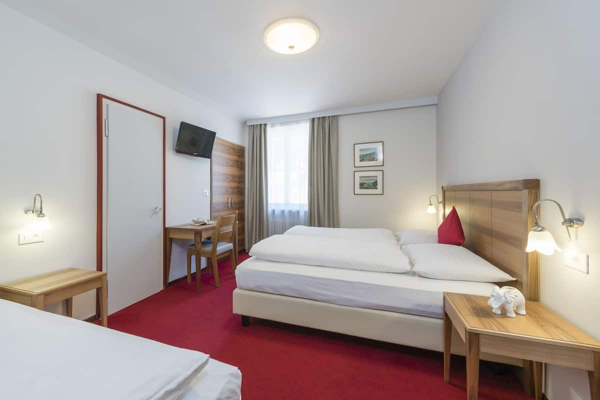 A hotel room with a bed, a desk, a chair, a TV, and a small table with a decorative elephant.