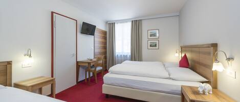 A hotel room with a bed, a desk, a chair, a TV, and a small table with a decorative elephant.