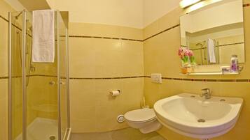 A bathroom with a glass shower enclosure, a toilet, and a sink with a mirror above.