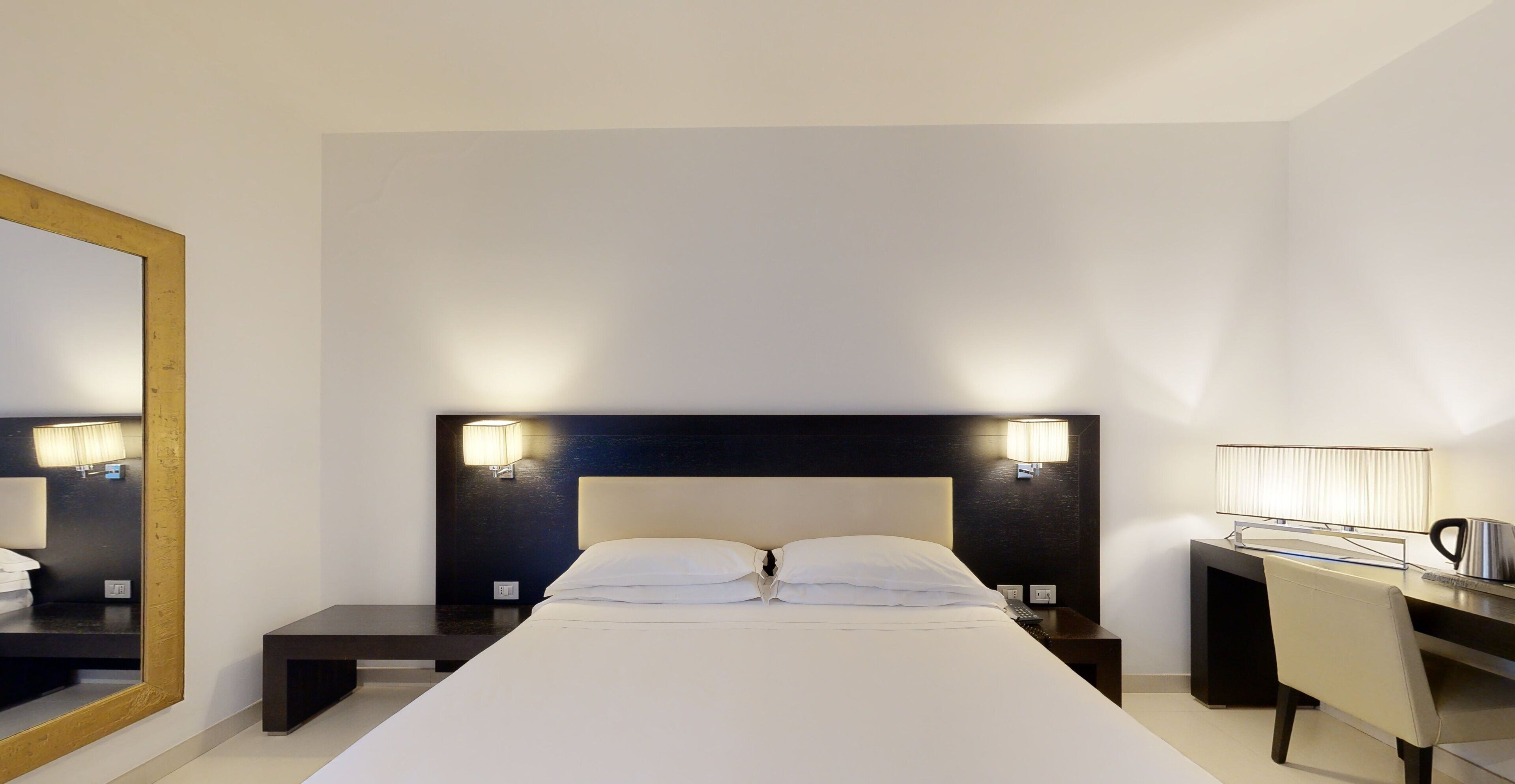 Une chambre d’hôtel avec un grand lit, des tables de chevet, un bureau avec une chaise et des lampes fixées au mur.