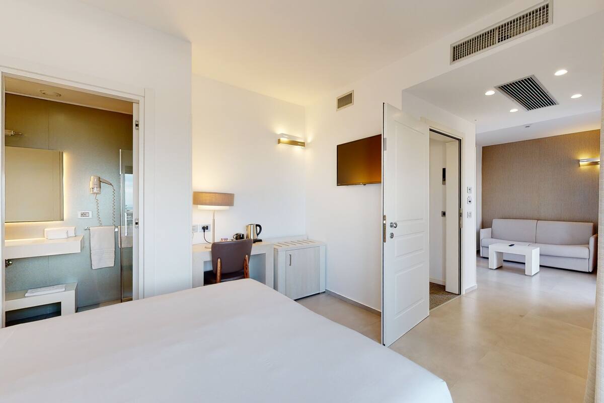 Una habitación de hotel moderna con una cama grande, un escritorio con silla, un sofá y un televisor.