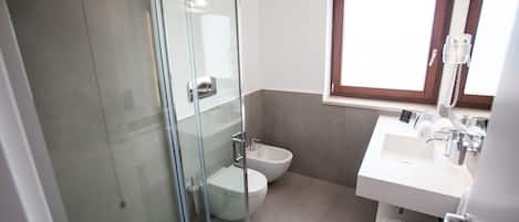 A modern bathroom with a glass shower enclosure, a toilet, and a sink with a window above it.
