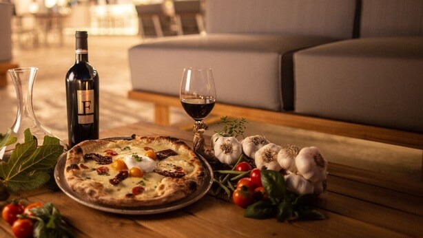 A dining table with a pizza, wine bottle, glasses, and fresh ingredients. - Hotel Monte Sarago (Ostuni)