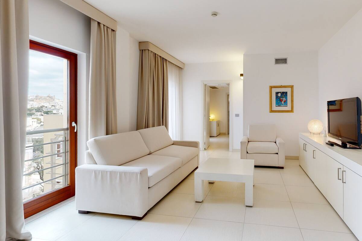 Una sala de estar moderna con un sofá, una mesa de centro, un televisor y vistas de la ciudad a través de amplios ventanales.
