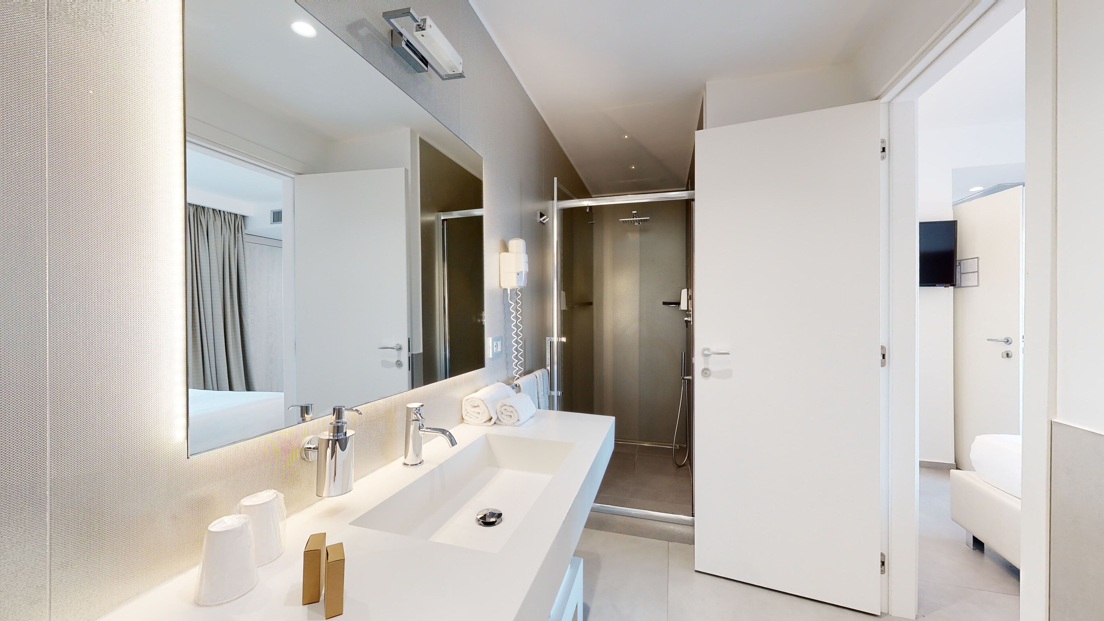 A modern bathroom with a long sink, a large mirror, and a shower area.