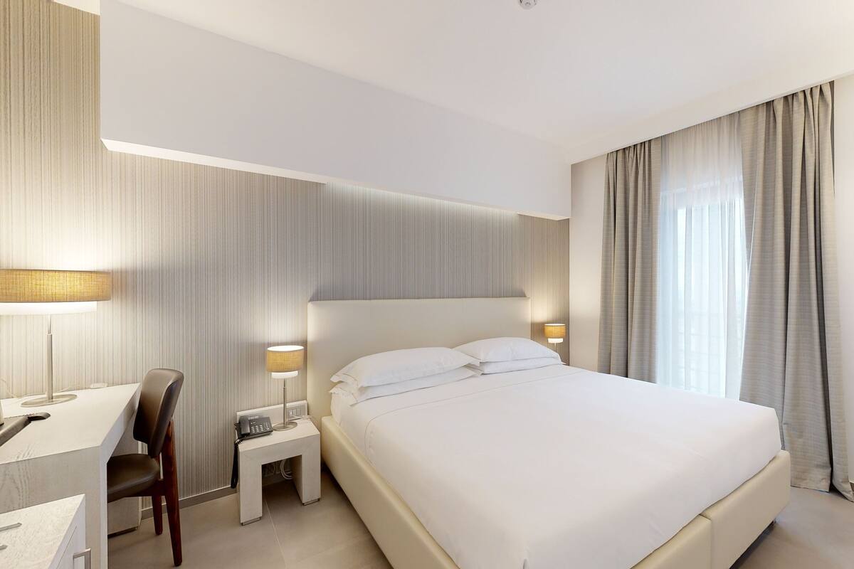 Una habitación de hotel con una cama, un escritorio, una silla, un teléfono y una lámpara.