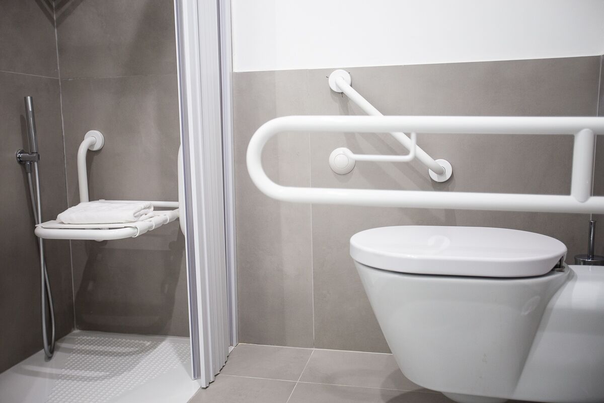 Un bagno moderno con doccia, toilette e maniglie di sostegno.