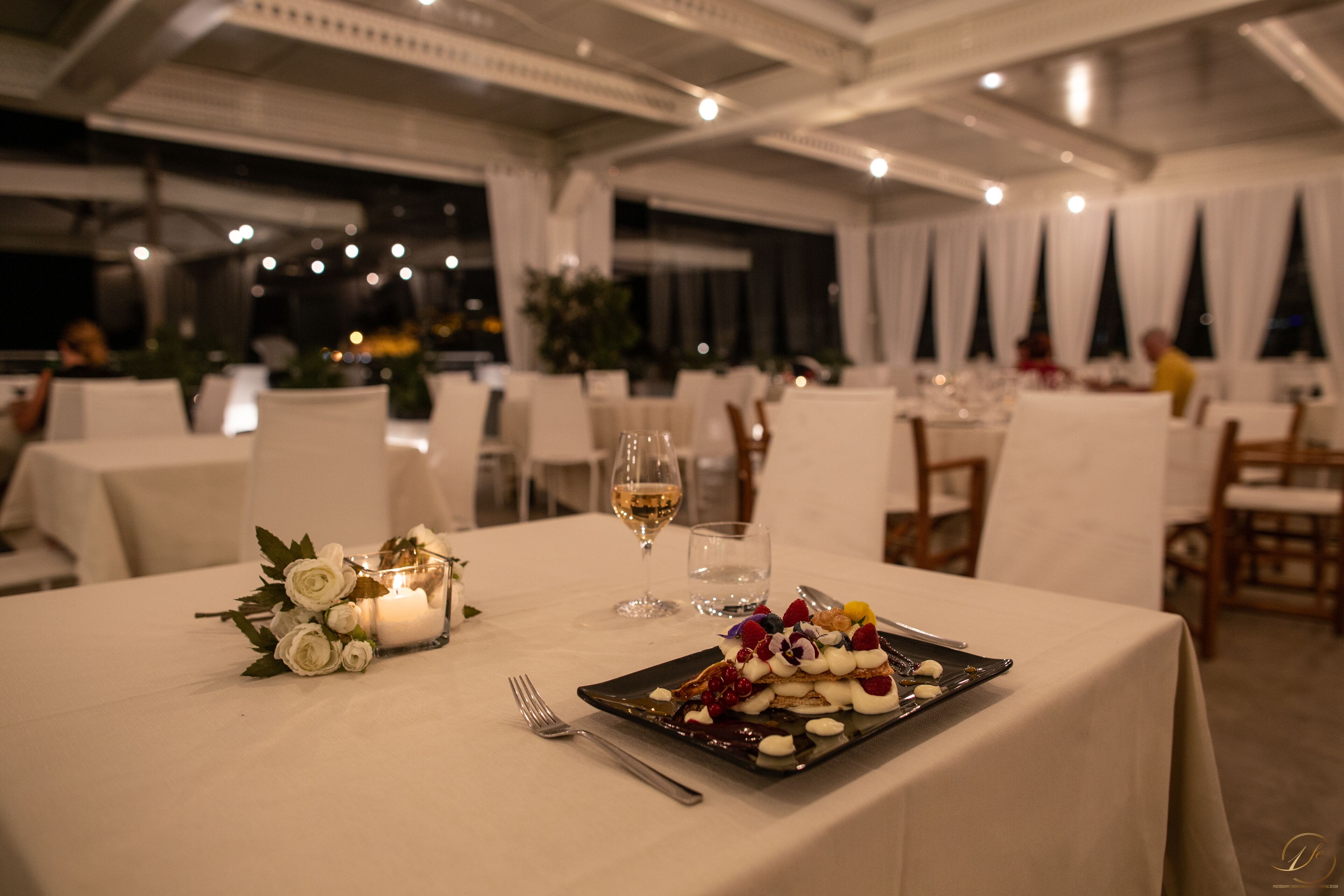 Une table à manger dressée avec des nappes blanches, des bougies et une assiette de nourriture.