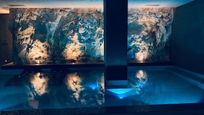 A modern indoor pool area with a large, textured wall and a central pillar. - Hotel Monte Sarago (Ostuni)