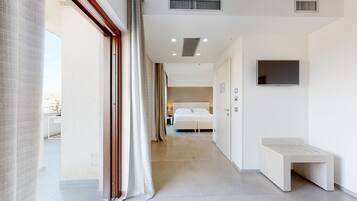Una habitación de hotel moderna con una cama grande, un banco y un televisor en la pared.