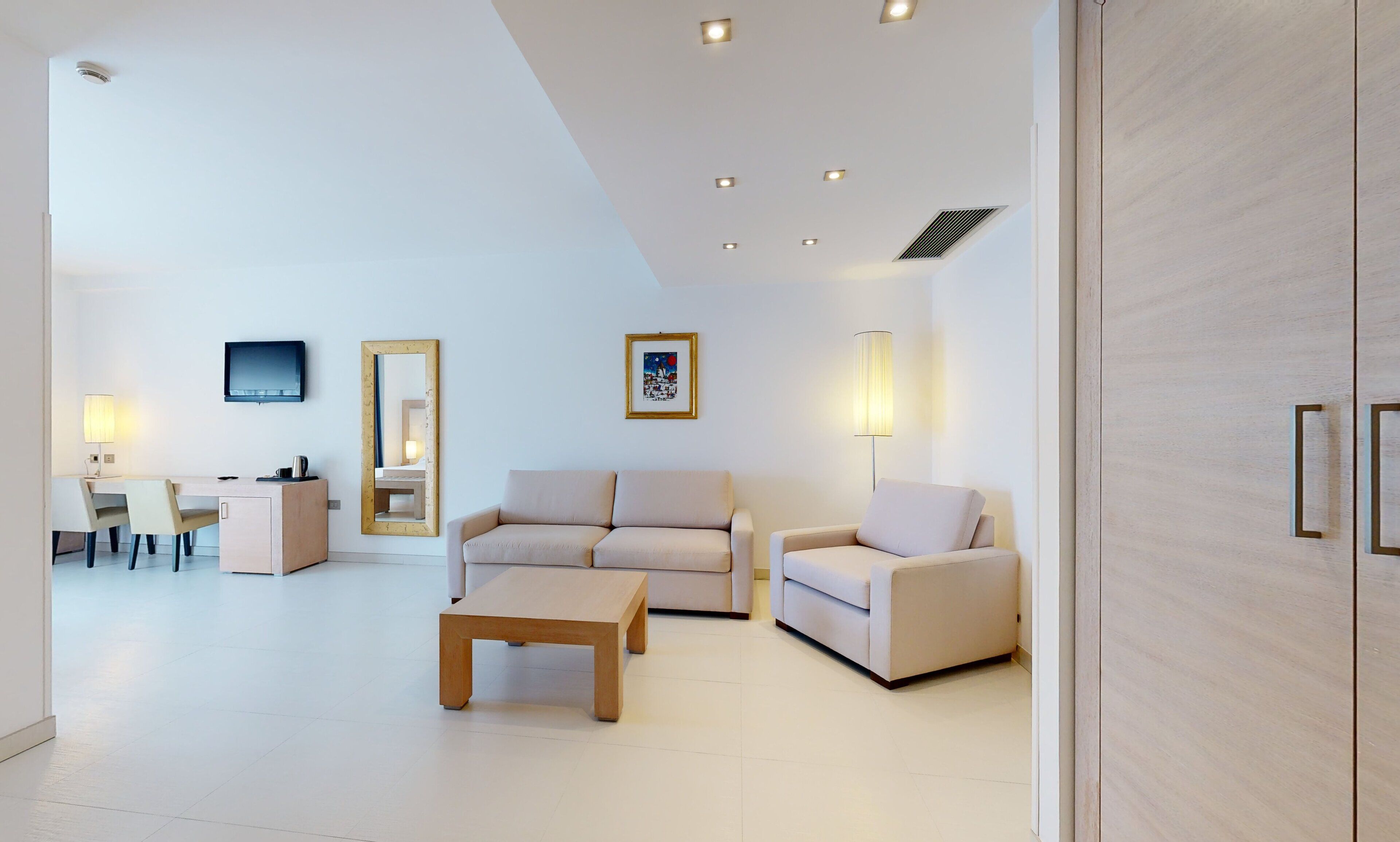 A modern living room with a sofa, two armchairs, a coffee table, a TV, and a dining area with chairs and a table.