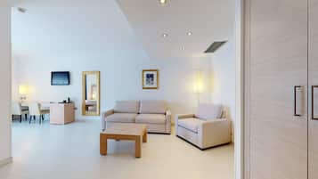 A modern living room with a sofa, two armchairs, a coffee table, a TV, and a dining area with chairs and a table.