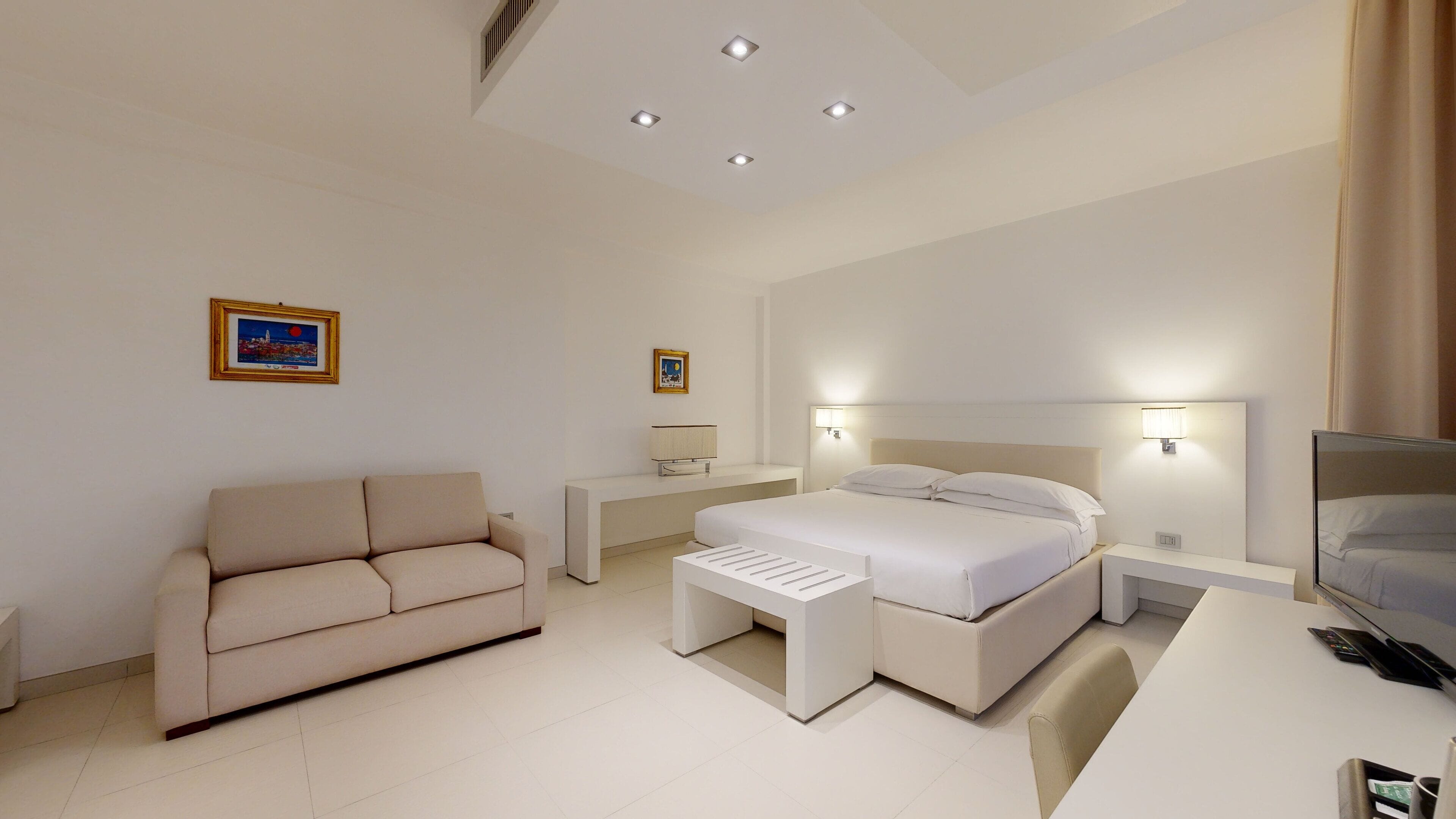 A modern hotel room with a bed, a sofa, a TV, and a desk.