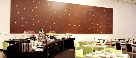 A modern dining area with a buffet setup, neatly arranged tables, and a large illuminated wall feature.