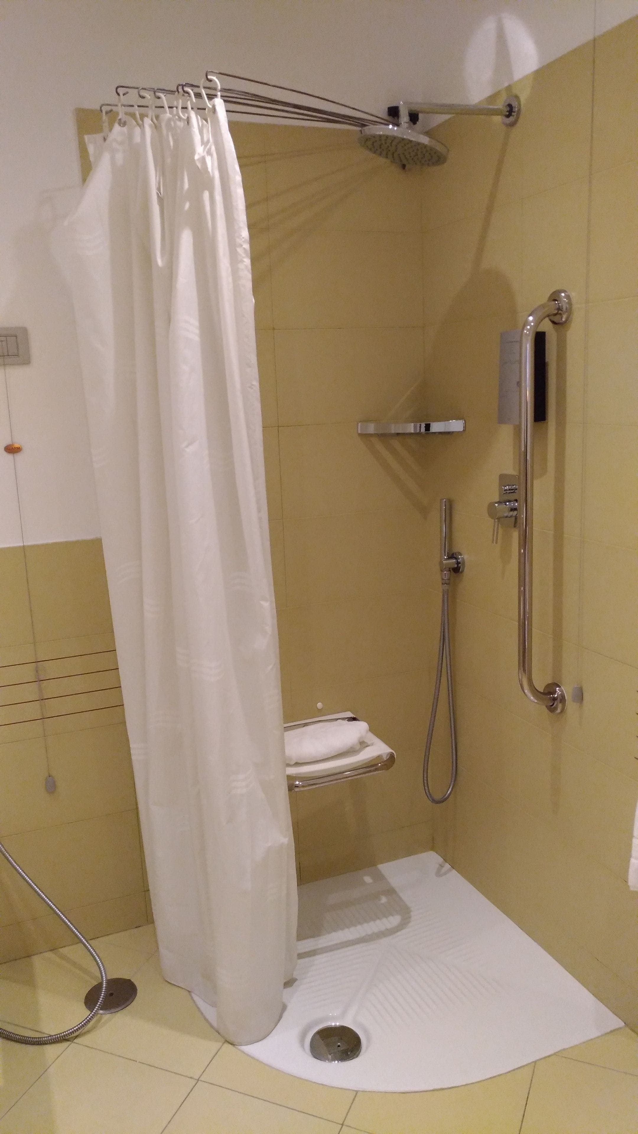 A small, enclosed shower area with a white shower curtain, a handheld showerhead, a handheld shower attachment, and a towel rack.