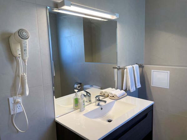A modern bathroom with a white sink, a mirror, a hairdryer, and a towel rack. - Royal Park Lodge (Auckland)