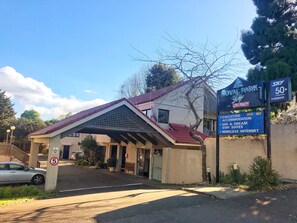 A hotel entrance with a covered walkway, a sign indicating a vacancy, and amenities listed such as executive accommodation, spa, and wireless internet. - Royal Park Lodge (Auckland)