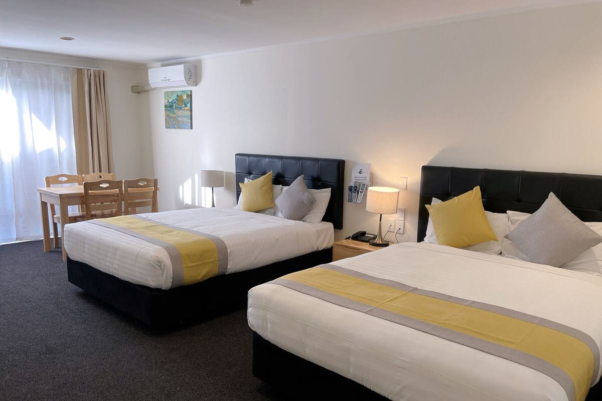 A hotel room with two beds, a desk, a chair, a lamp, and a painting on the wall.