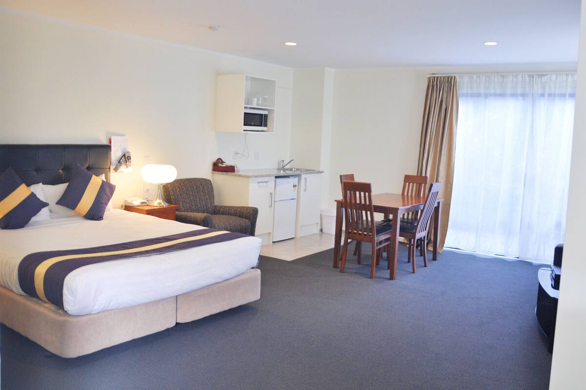 A hotel room with a bed, a desk, a chair, a microwave, and a dining table.