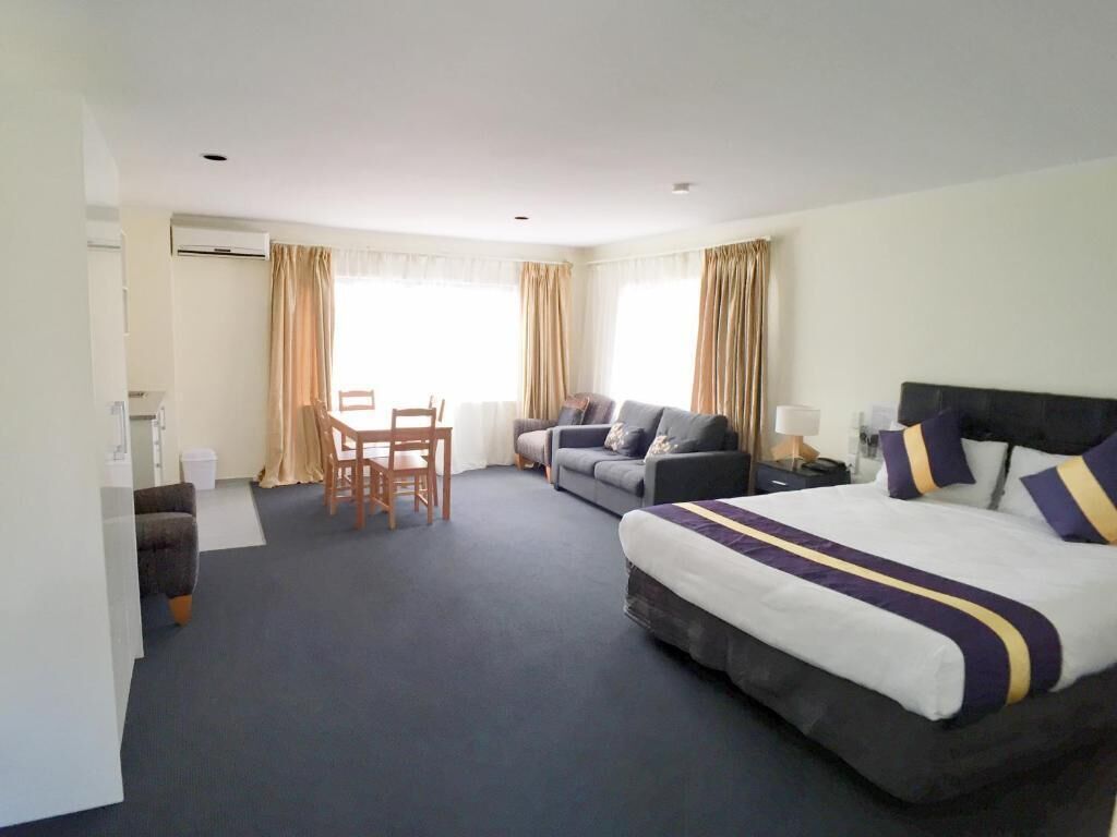 A hotel room with a large bed, two sofas, a dining table, and a chair. - Royal Park Lodge (Auckland)